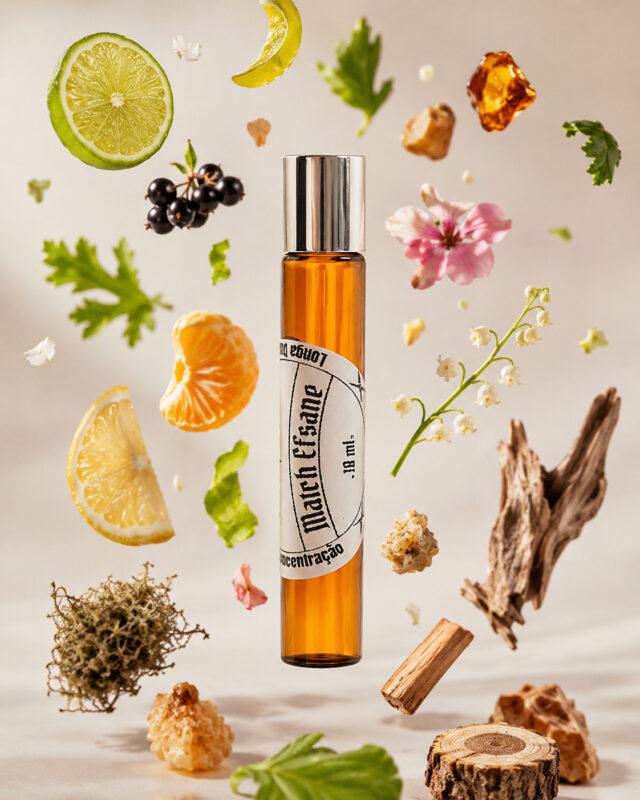 frasco de perfume âmbar de vidro modelo roll on com tampa cromada na posição vertical no centro rodeado por fatia de limão e laranja gomo de tangerina laranja madeira de cedro fava de baunilha hortelã