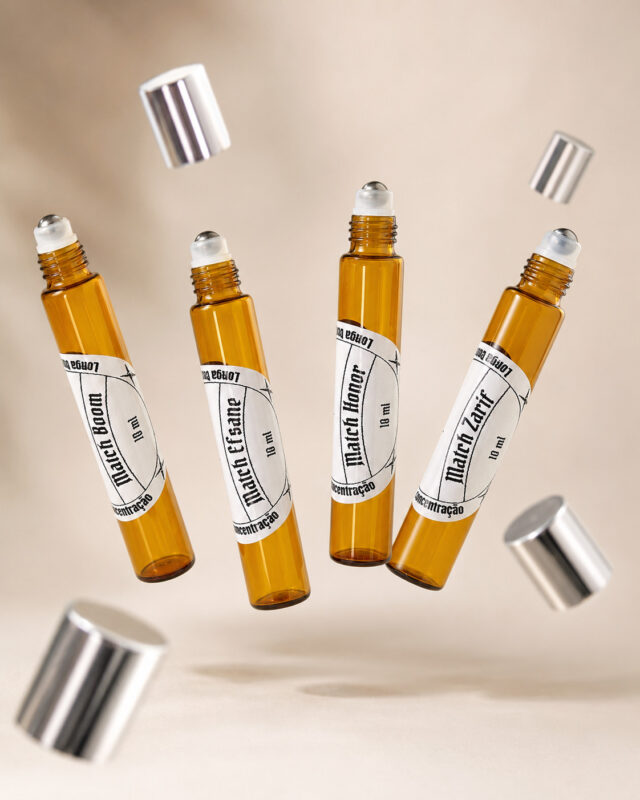 quatro frascos de perfume de bolsa feitos com vidro âmbar e pontas redondas com esferas de aço deslizantes dispostos lado a lado flutuando com tampas prateadas pairando sobre o ar