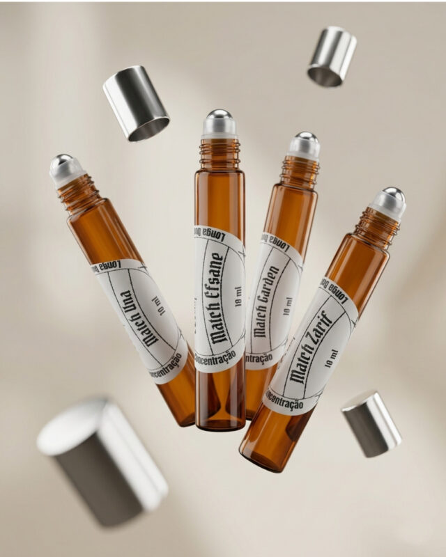 quatro frascos cilíndricos de perfume portátil feitos em vidro âmbar com pontas de esfera de aço deslizantes aparentes dispostos lado a lado com tampas prateadas soltas