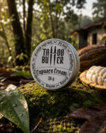 Latinha de alumínio Tattoo Butter Cupuaçu Cream com rótulo branco redondo em destaque, apoiada sobre musgo ao lado de um fruto de cupuaçu aberto em ambiente de floresta.