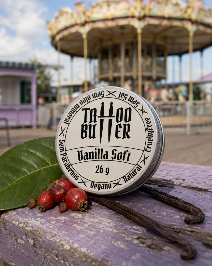 latinha de alumínio com rótulo branco redondo tattoo butter vanilla soft 26g sob tampo de madeira violeta claro descascado com folha verde e frutas vermelhas ao fundo carrossel e montanha russa