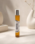 Frasco cilíndrico de perfume portátil feito em vidro âmbar com rótulo branco match bee na posição vertical sob pedra de granito bege