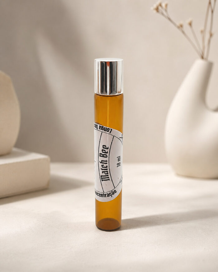 Frasco cilíndrico de perfume portátil feito em vidro âmbar com rótulo branco match bee na posição vertical sob pedra de granito bege