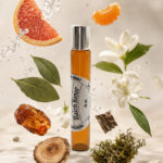 frasco âmbar de perfume portátil na posição vertical no centro da imagem rodeado por gomo de tangerina âmbar cedro lírio hotelã pedaço de toranja