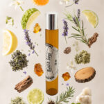 frasco de perfume portátil cilíndrico de vidro âmbar com tampa cromada com rótulo redondo branco match soul na vertical rodeado por fatia de limão pedaço de madeira de cedro alecrim lavanda gomo de tangerina âmbar